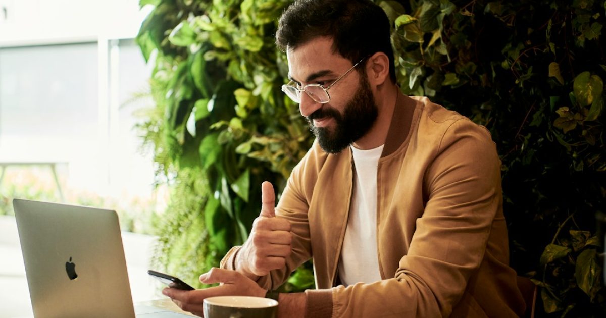 Jovem empreendedor a trabalhar no seu portátil num café moderno, simbolizando o início de um negócio digital de hosting com baixo investimento.