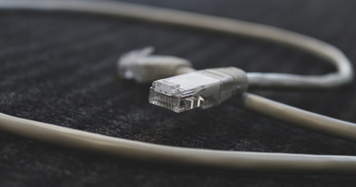 Cabo Ethernet conectado a um portátil, router Wi-Fi ao fundo, comparando ligações para baixa latência.